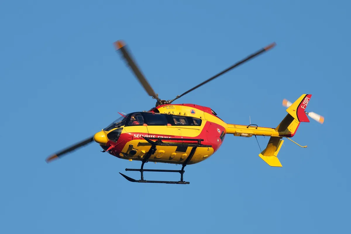 Hélicoptère jaune et rouge de la Sécurité civile en vol sur fond de ciel bleu