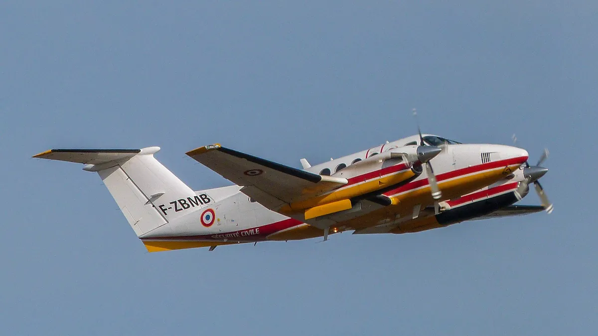 Beechcraft King Air F-ZBMB de la Sécurité civile en vol, train sorti, sur un ciel gris bleu